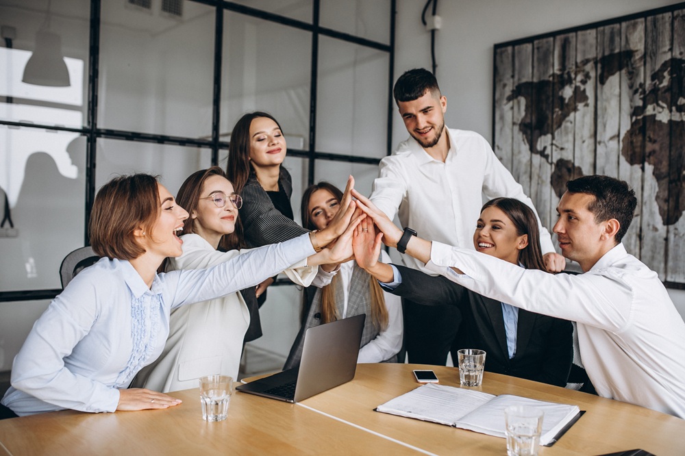 Group of business professionals in a meeting room doing a team high-five around a conference table.