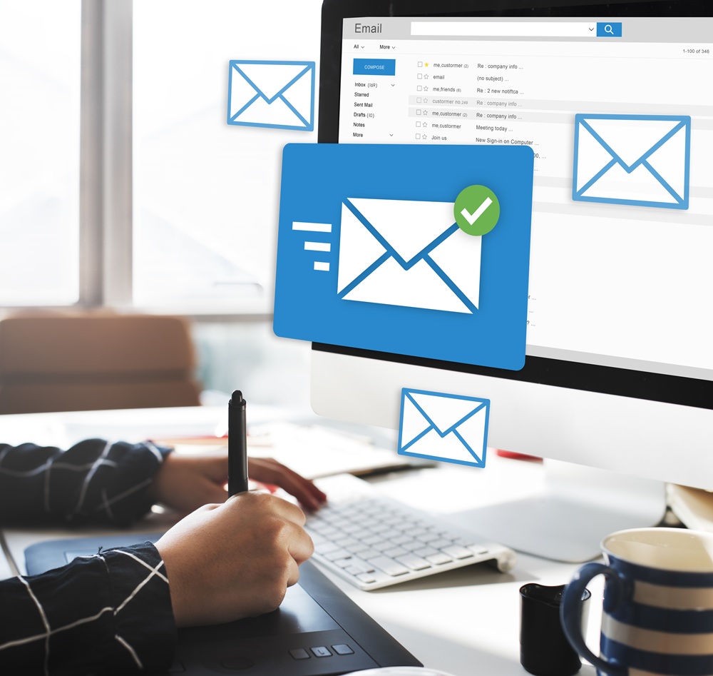 Person working at a desk with email icons floating around a computer screen displaying an email inbox.