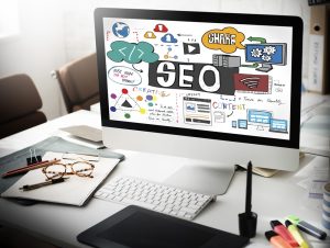 Desktop computer on a workspace displaying a colorful SEO and digital marketing strategy diagram with icons and keywords.